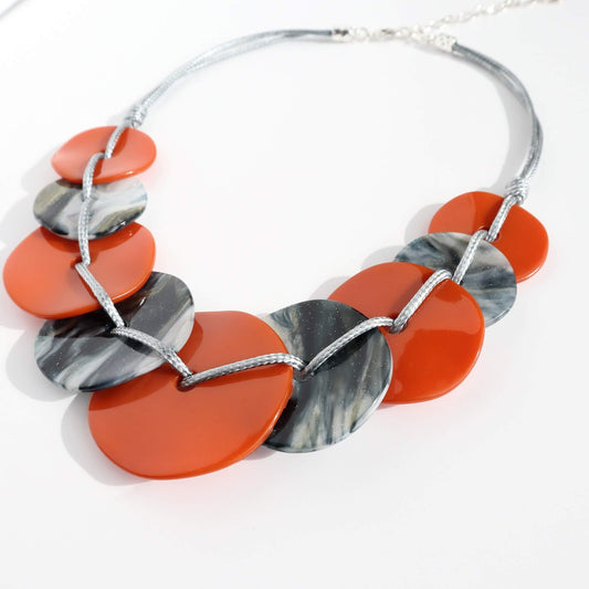 Close-up of a lightweight statement necklace with alternating orange and grey marbled flat circular beads. Connected by silver-toned wire.