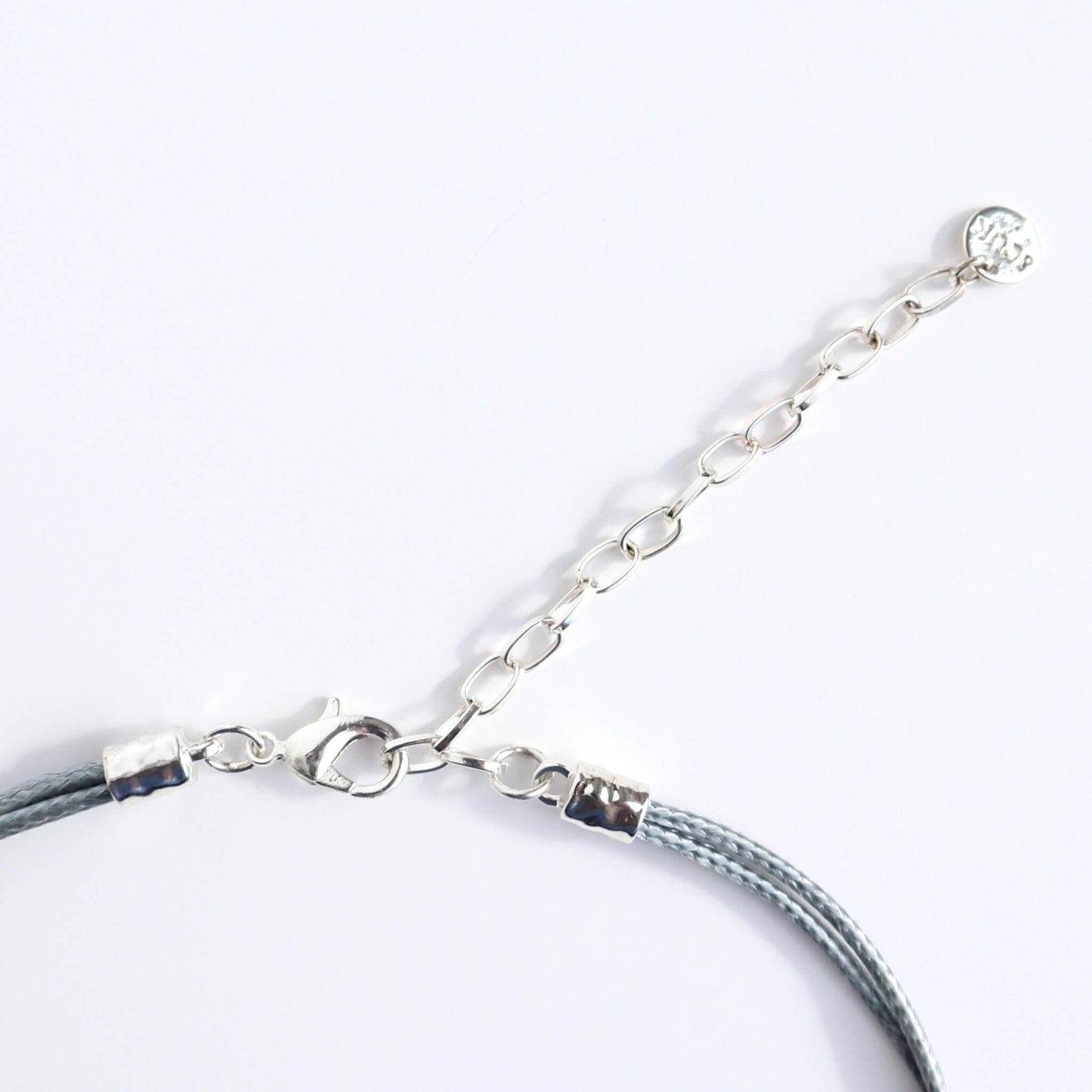 Close-up of a silver-toned statement necklace clasp and extender chain. Features a lobster claw closure and a small round charm. Grey wire is visible.