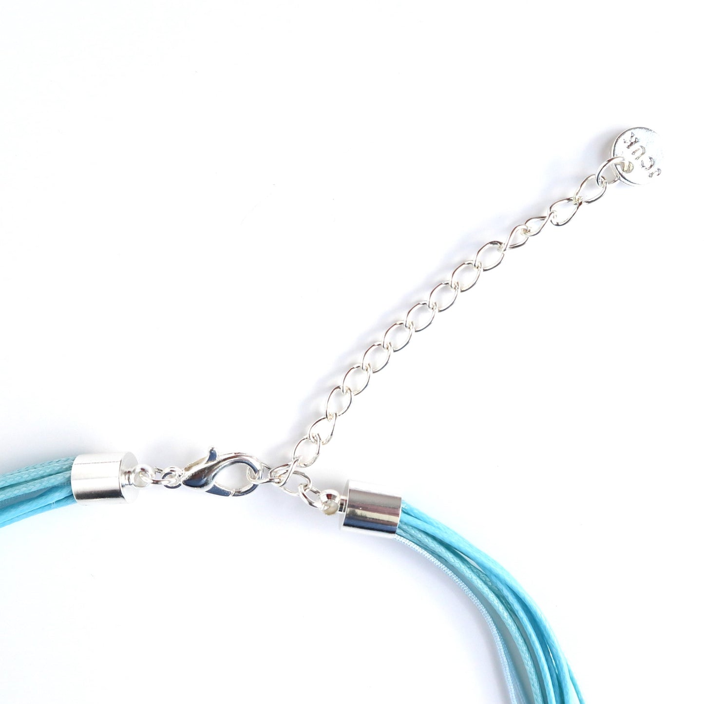 Close-up of a teal cord necklace clasp and extender chain in silver-tone metal. Multiple cords are secured with silver caps.