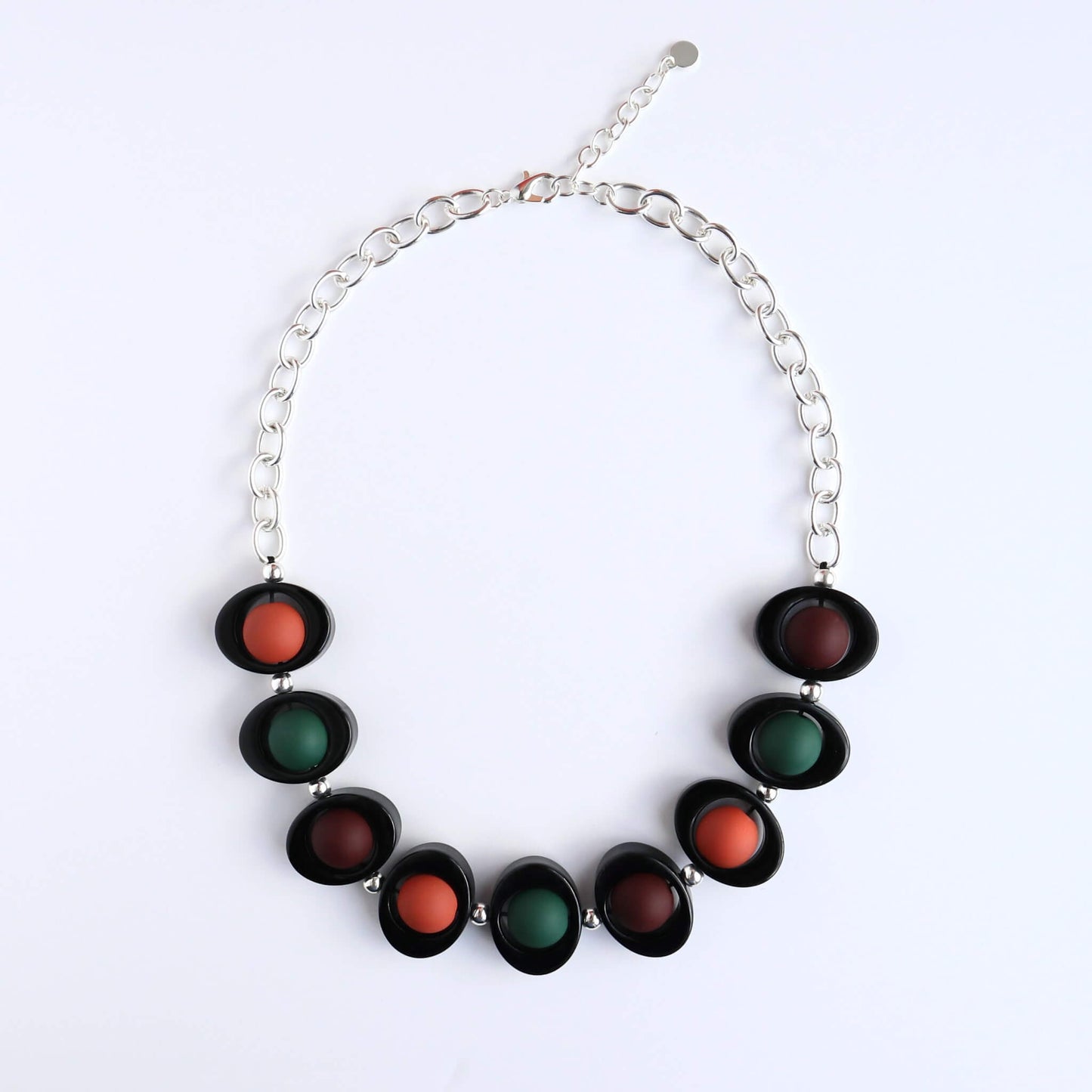Chunky statement necklace with black oval frames holding matte burnt orange, dark green, and deep red round beads. Silver-tone chain and clasp.