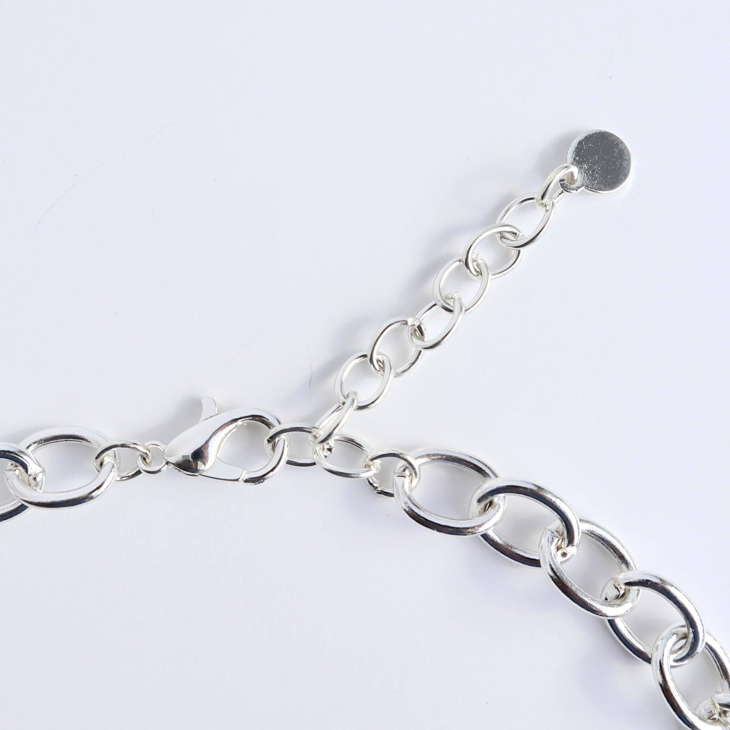Close-up of a silver-toned statement necklace clasp and extender chain. Features a lobster claw closure and a small circular charm.