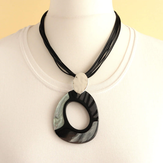 Modern statement necklace with a large, glossy black and grey swirl pendant. Features a smaller, brushed silver oval detail and multiple black cords.