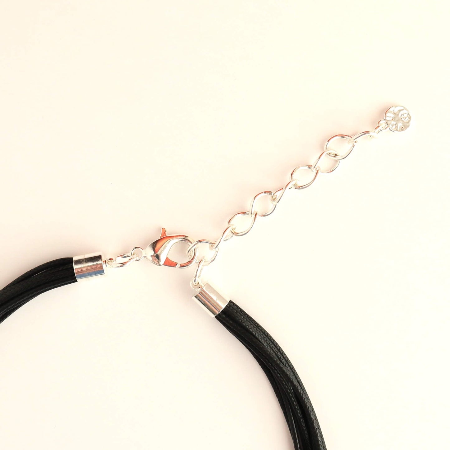 Close-up of a silver-toned statement necklace clasp and extender chain. Features a lobster claw closure and a small decorative charm. Black cords are visible.