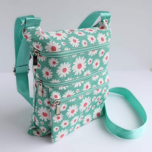 Mint green crossbody bag with a white and pink daisy pattern. Features three zippered sections and a matching adjustable shoulder strap.