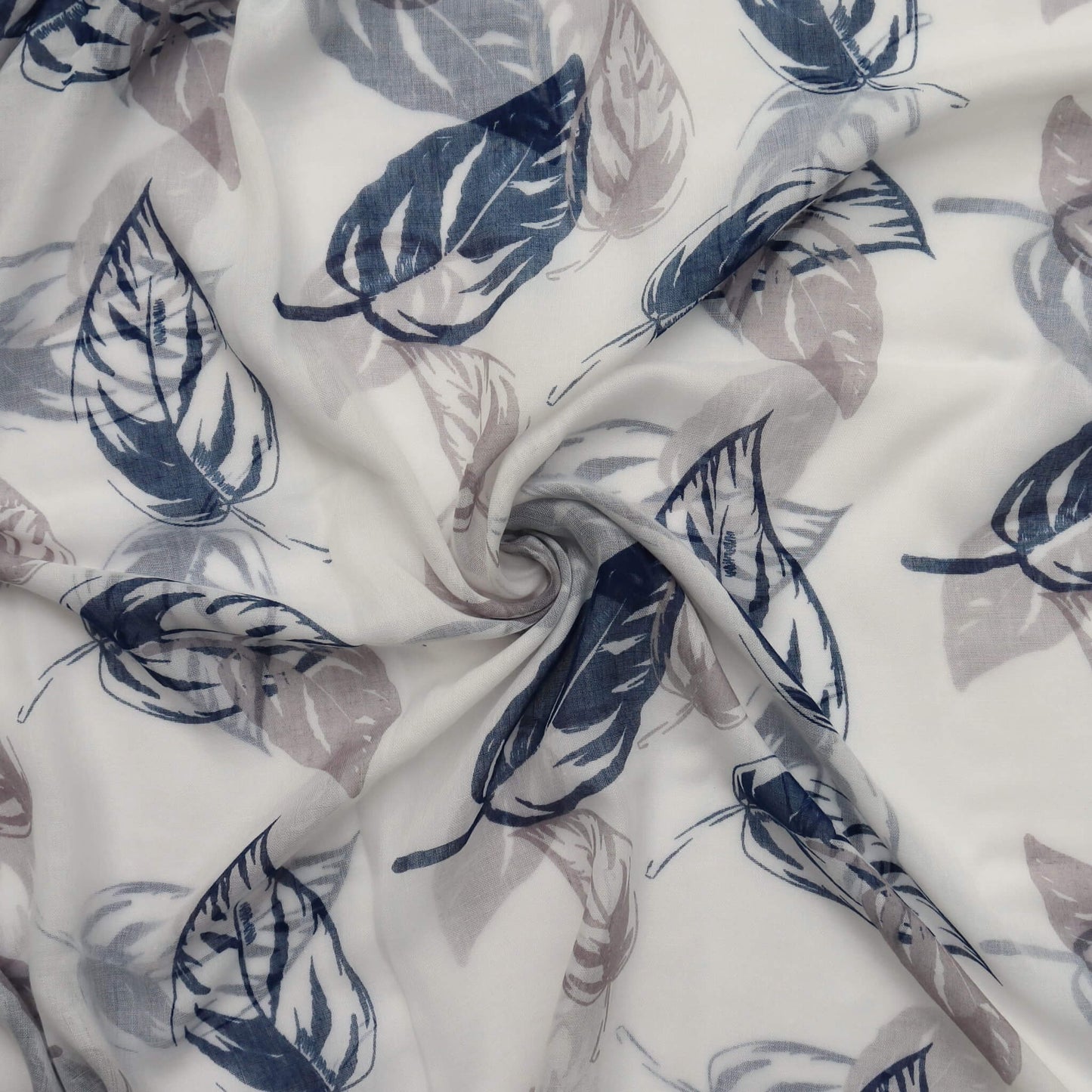 Aurora's Array: Close-up of a soft, lightweight white scarf with a large leaf print in shades of grey and navy blue, swirled to show detail.