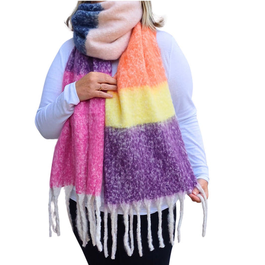 Aurora's Array: Woman models a vibrant rainbow striped cosy blanket scarf with chunky tassels, suggesting a warm and colourful gift.