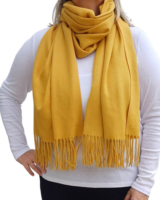 Aurora's Array: Woman models a soft, warm mustard yellow wool blend scarf with fringed edges, draped around her neck and shoulders.