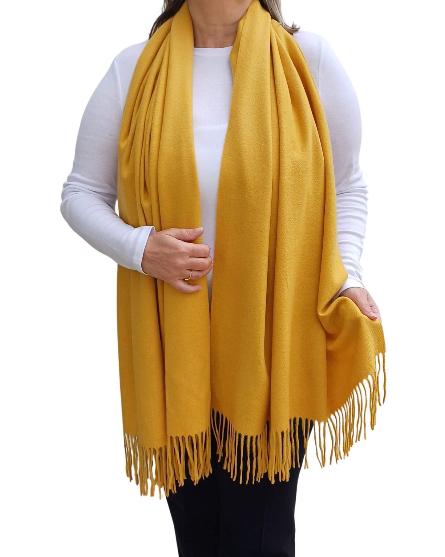 Aurora's Array: Woman models a soft, warm mustard yellow wool blend scarf with fringed edges, draped around her neck and shoulders.