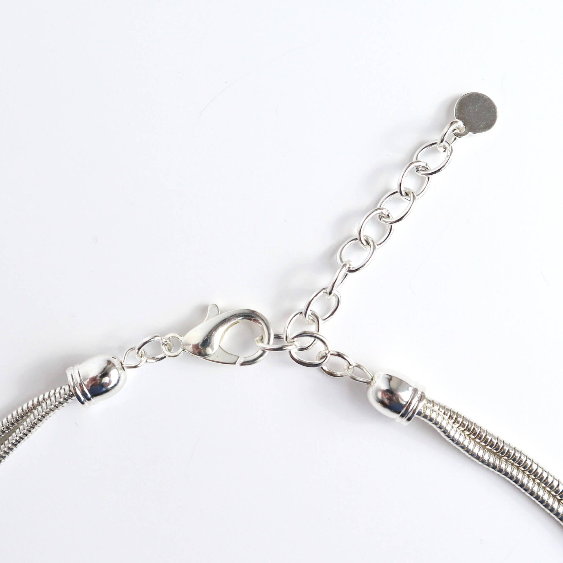 Close-up of a silver-toned necklace clasp and extender chain. Features a lobster claw closure and a small circular charm at the end of the chain.