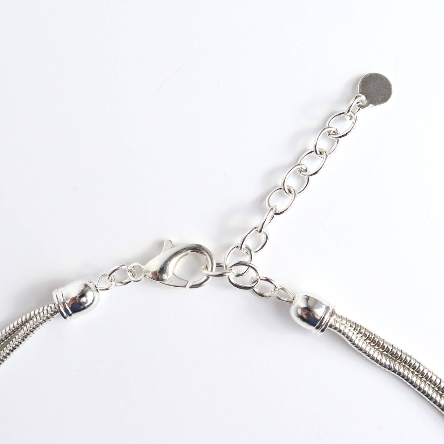 Close-up of a silver-toned necklace clasp and extender chain. Features a lobster claw closure and a small circular charm at the end of the chain.