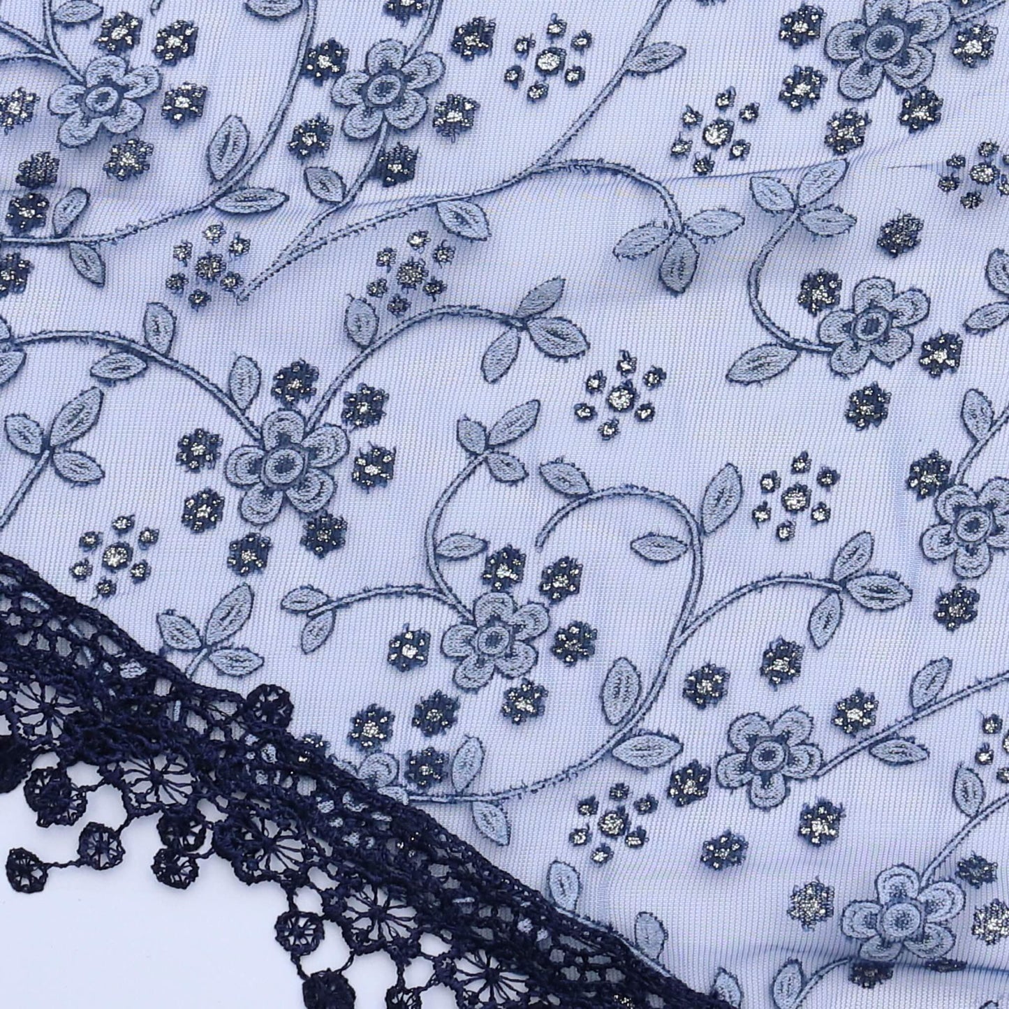 Aurora's Array Glitter Triangle Scarf with Lace & Embroidery (Close-up): A detailed close-up of a dark blue, sheer fabric with delicate white floral embroidery accented with subtle glitter. The edge features intricate dark blue lace trim with dangling emb