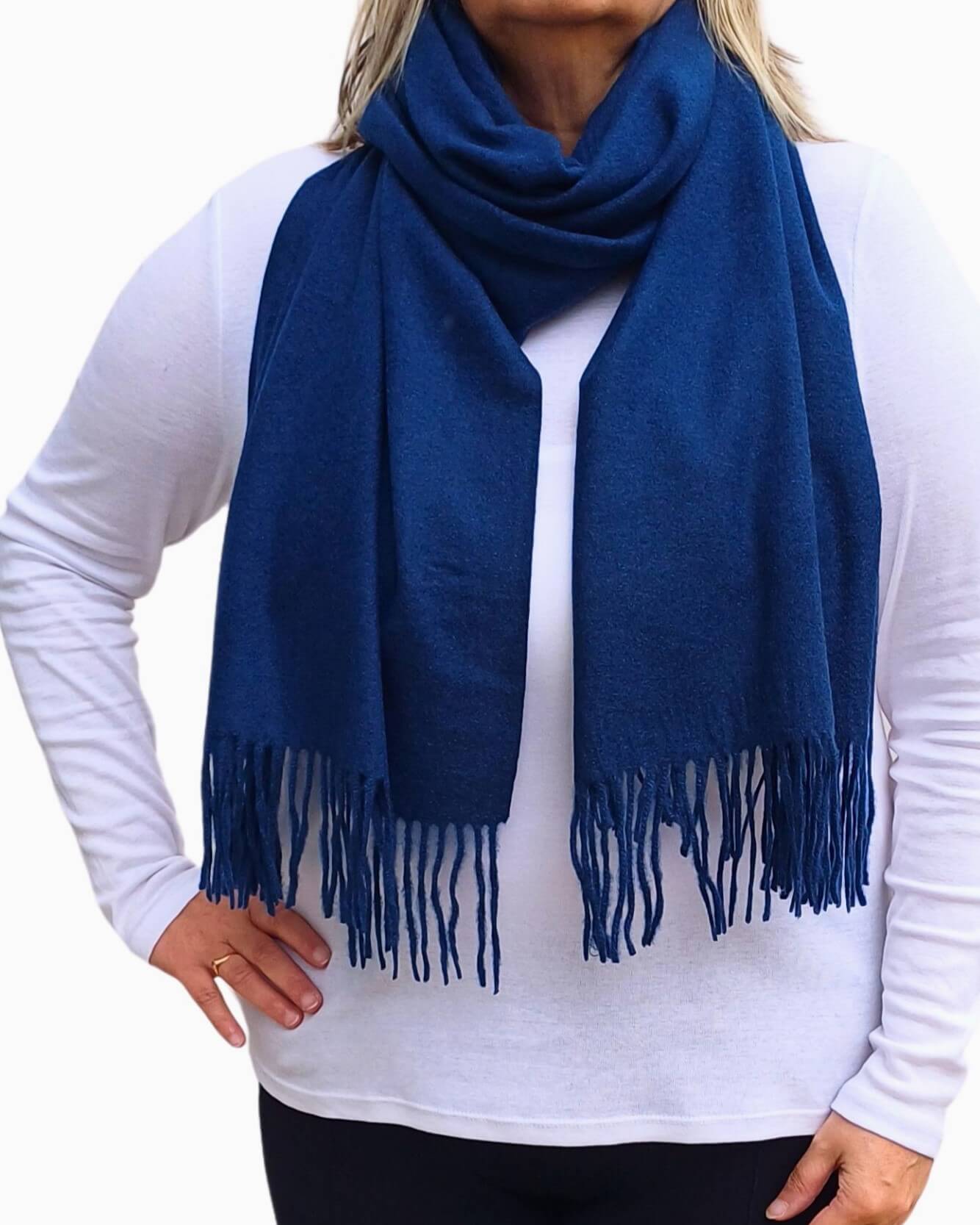 Aurora's Array: Woman models a soft, warm navy blue wool blend scarf with fringed edges, draped around her neck and shoulders.