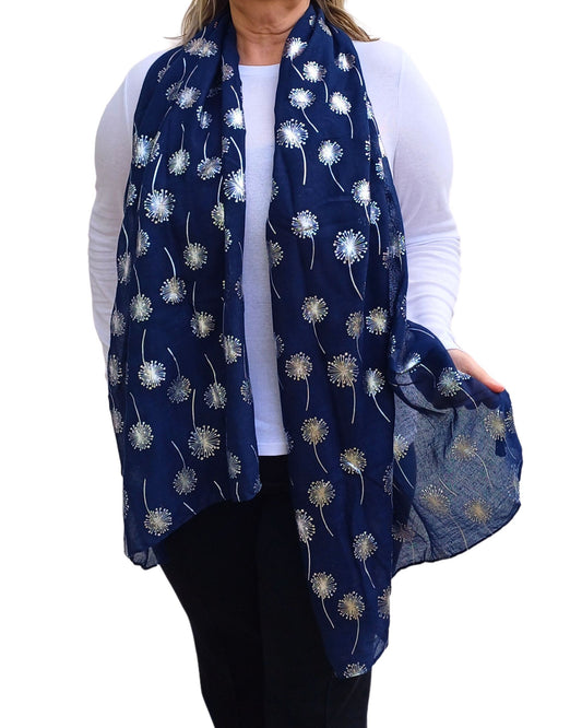 A person wearing a navy blue scarf with a metallic silver foiled dandelion print, paired with a white top and black pants.