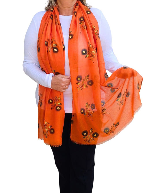 Aurora's Array: Woman models a soft, lightweight bright orange scarf with a small black and gold floral print.