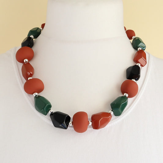 Short beaded necklace with matte rust-orange, shiny black, and glossy dark green irregular shaped beads, separated by small silver-tone spacers.