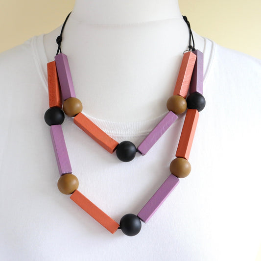 Modern black cord necklace featuring matte lavender and orange rectangular wood beads, plus smooth tan and black round wood beads.