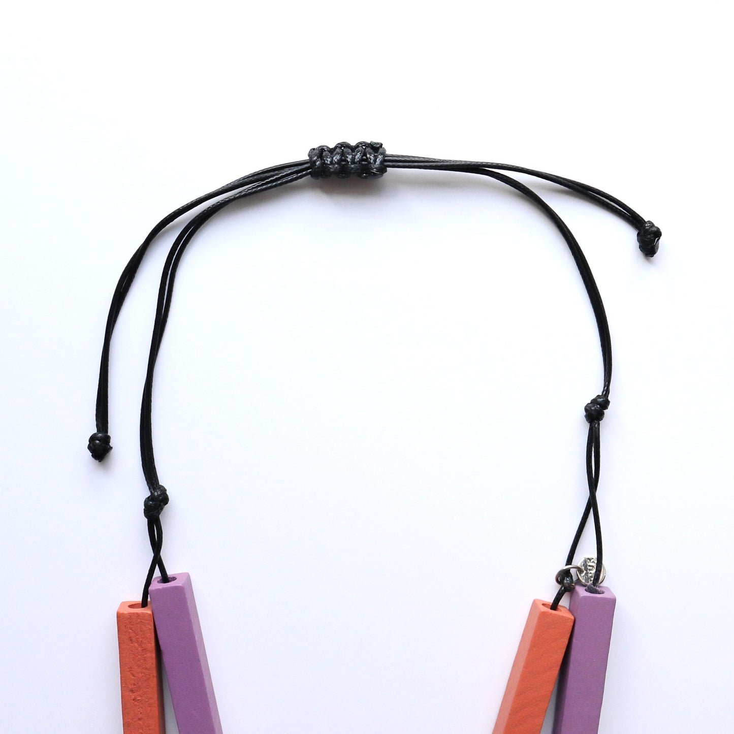 Close-up of the adjustable black cord closure of a geometric necklace. Features a sliding knot and visible matte orange and lavender wooden beads.