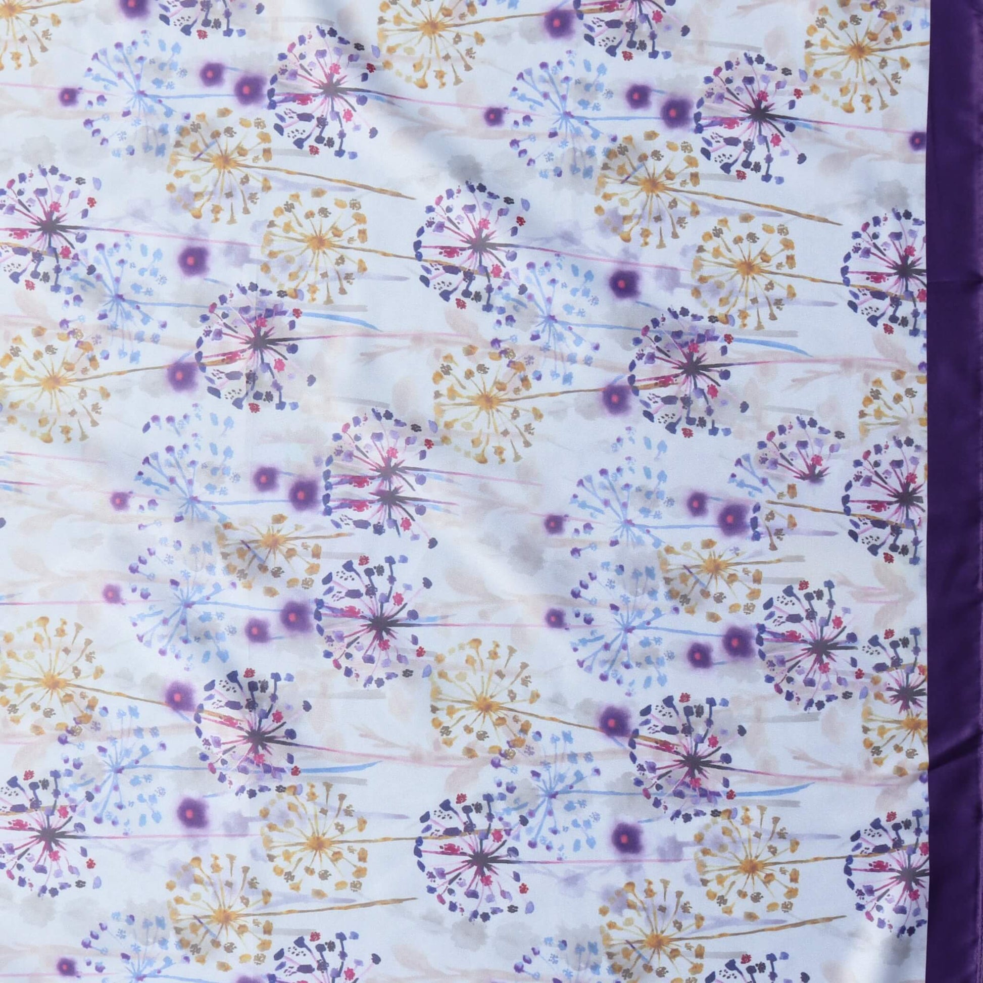 Aurora's Array: Close-up of a light satin scarf with a delicate dandelion and wildflower print in shades of purple, blue, and white, bordered by a deep purple satin edge on the right.