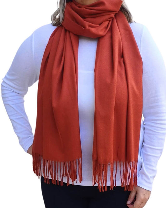Aurora's Array: Woman models a soft, warm rust orange wool blend scarf with fringed edges, wrapped around her neck.