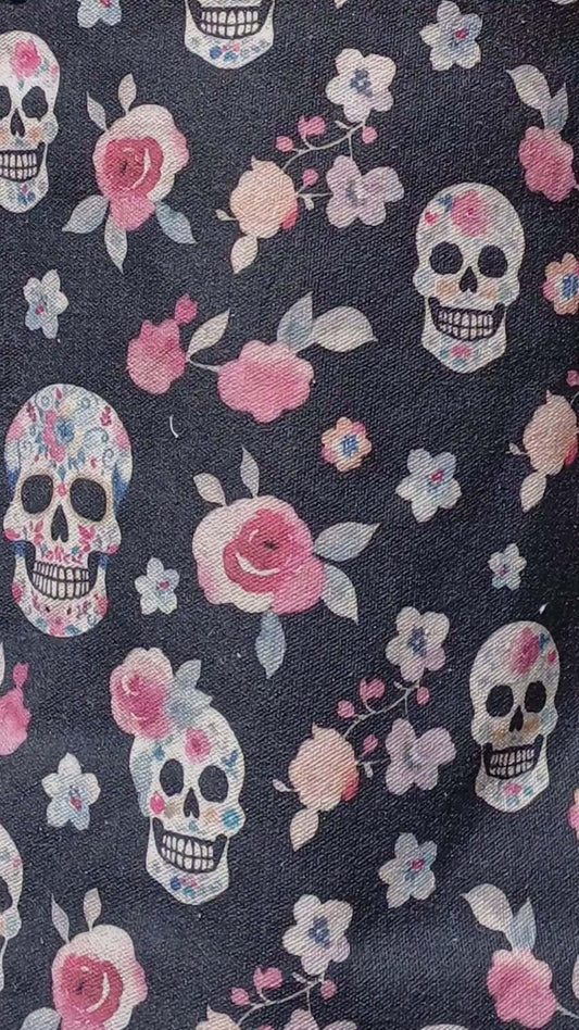 Close-up of a dark grey canvas tote bag's design: a pattern of decorated skulls and pink floral elements. Detailed print.