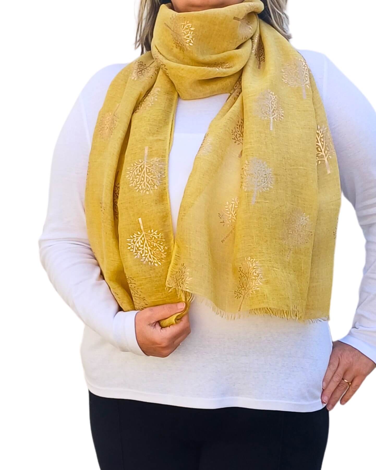 Aurora's Array: Woman models a soft, mustard yellow scarf with a subtle gold tree print and frayed edges, wrapped around her neck.