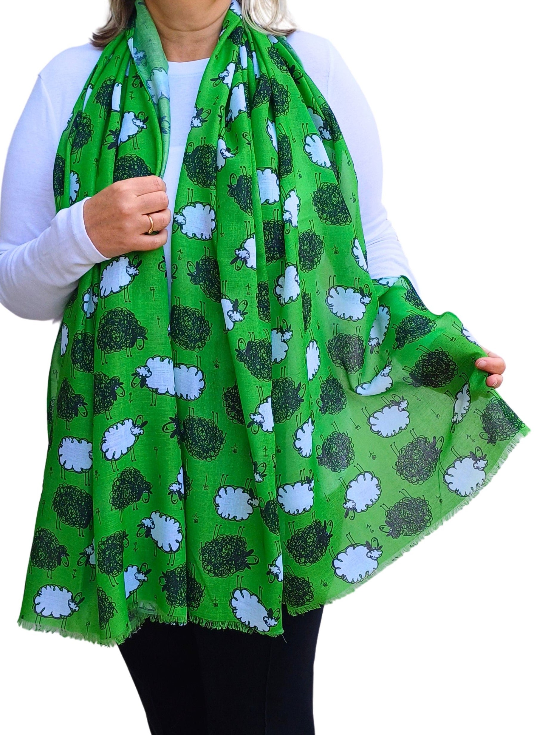 A vibrant green scarf with playful black and white sheep illustrations. Soft, draped fabric with a subtle fringe.