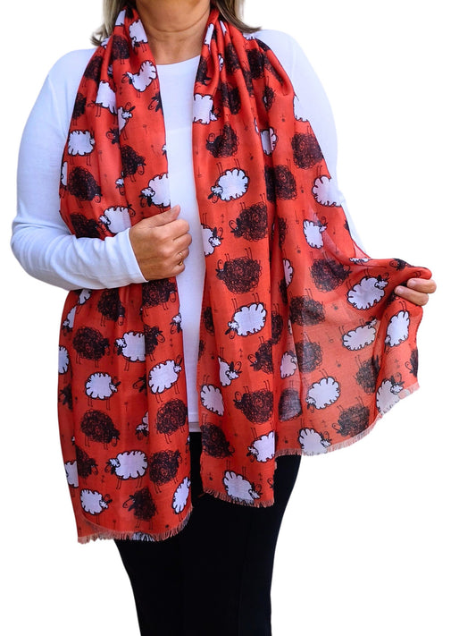 A vibrant red scarf featuring whimsical black and white sheep designs. Soft, flowing fabric with a delicate fringed edge.