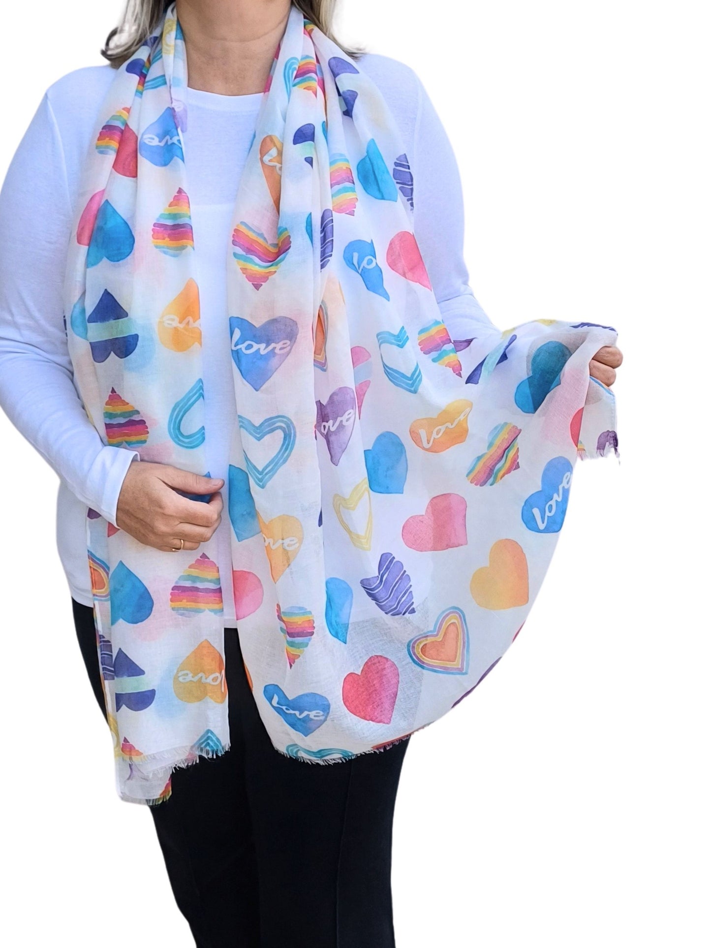 Aurora's Array Watercolour Hearts Scarf: A woman wearing a white long-sleeved top and black trousers models a soft, lightweight white scarf printed with colourful watercolour-style hearts and the word "love"