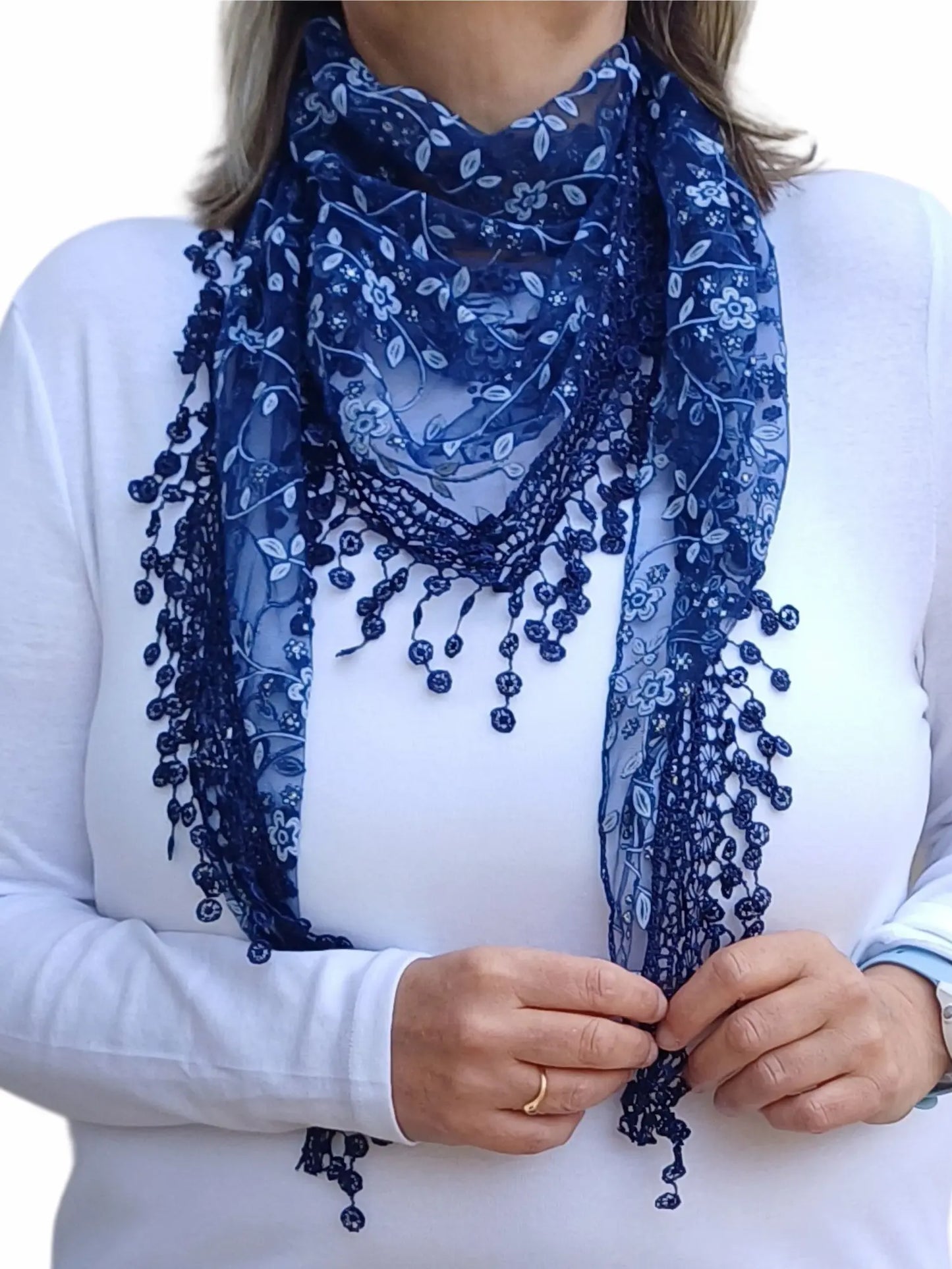 Aurora's Array Glitter Triangle Scarf with Lace & Embroidery: A woman models a dark blue, sheer triangle scarf with a delicate white floral print, intricate lace trim, and dangling embroidered accents.