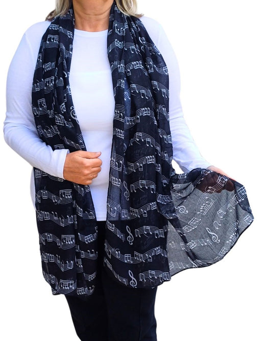 Lightweight black scarf adorned with an all-over print of white musical notes, clefs, and staves. Soft, flowing fabric.