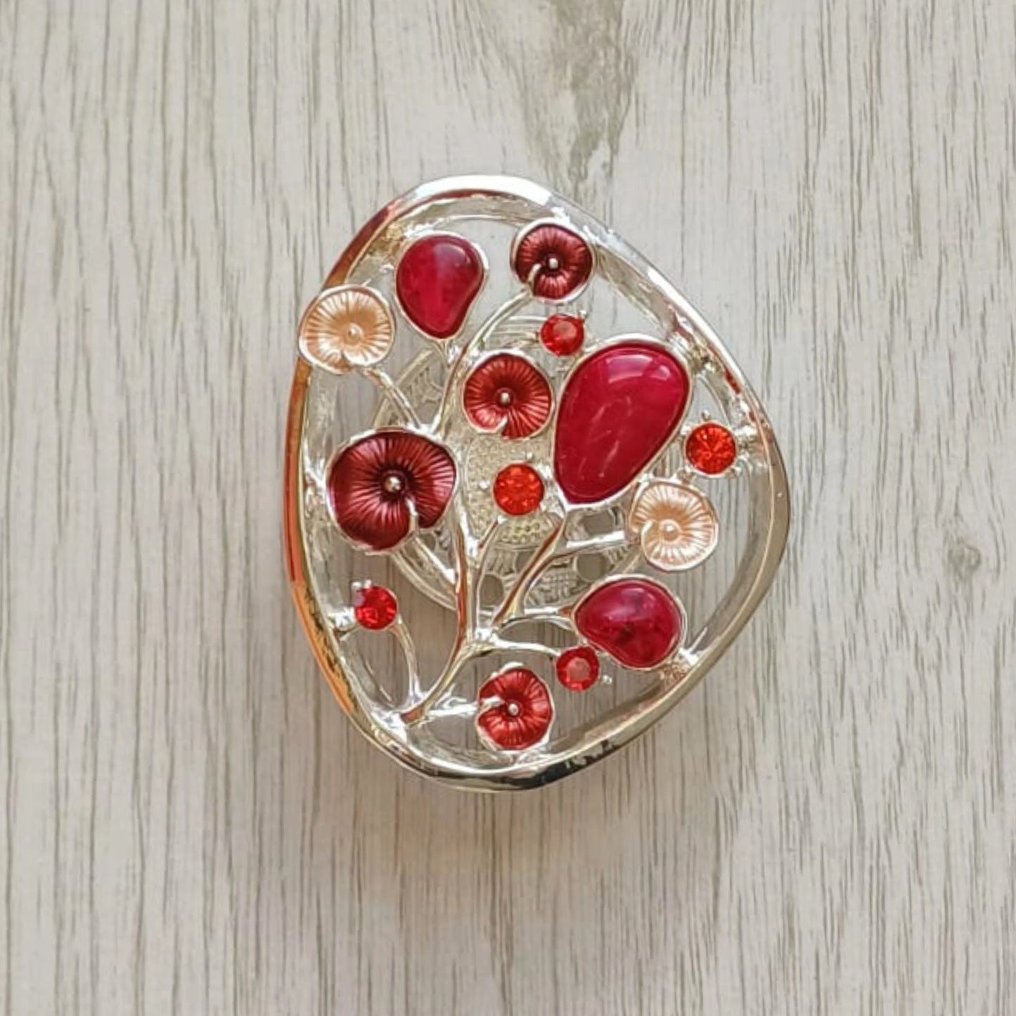 Red Tree of Bloom magnetic brooch with painted metal finish on pale wood surface