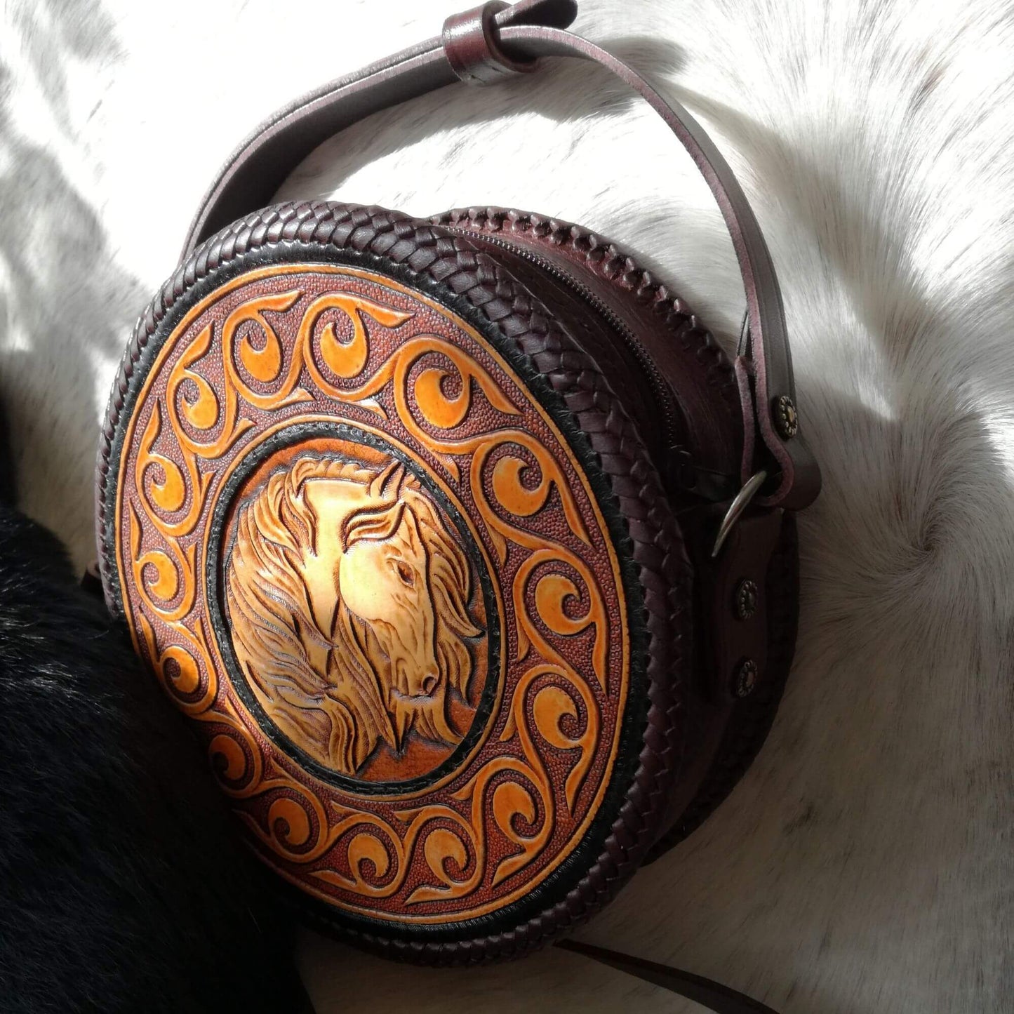 Angled front view of round leather crossbody bag with hand-tooled horse design – Equina