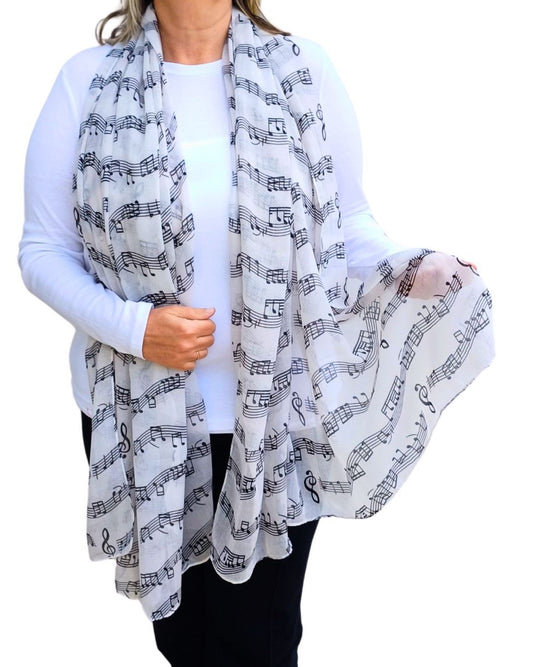 Delicate white scarf featuring a repeating pattern of black musical notations, including notes, clefs, and staff lines. Airy, flowing material.