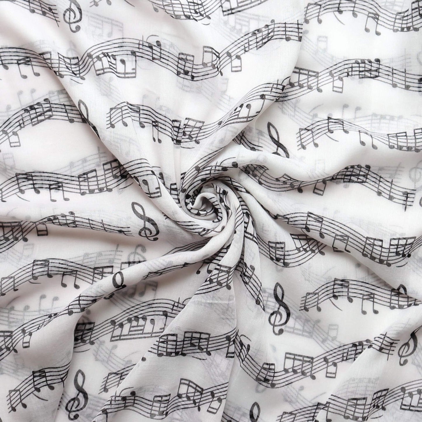 Delicate white scarf material with a repeating design of black musical symbols including notes, clefs, and staff lines. Airy, flowing feel.