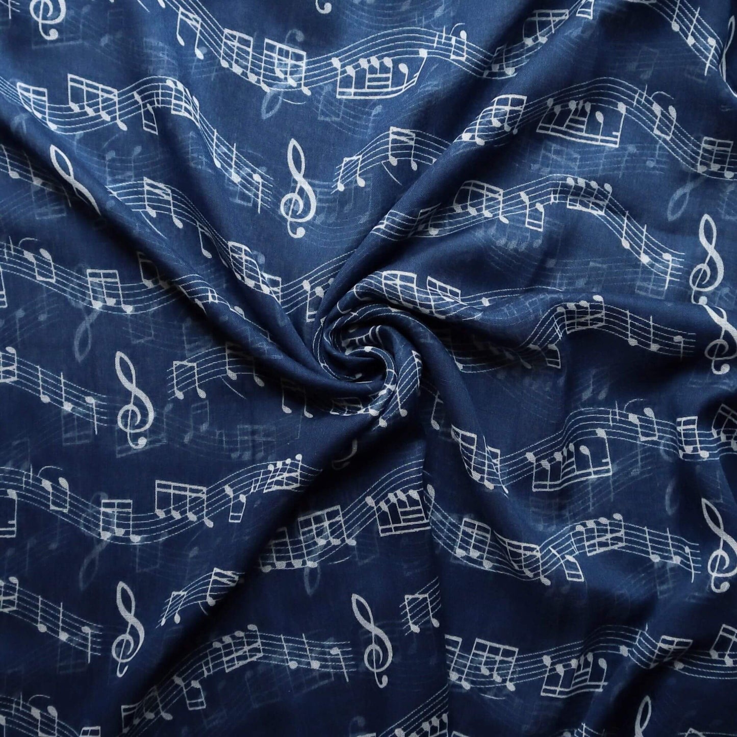 Soft navy blue scarf fabric with a repeating pattern of white musical symbols like notes, clefs, and staves. Lightweight, flowing texture.