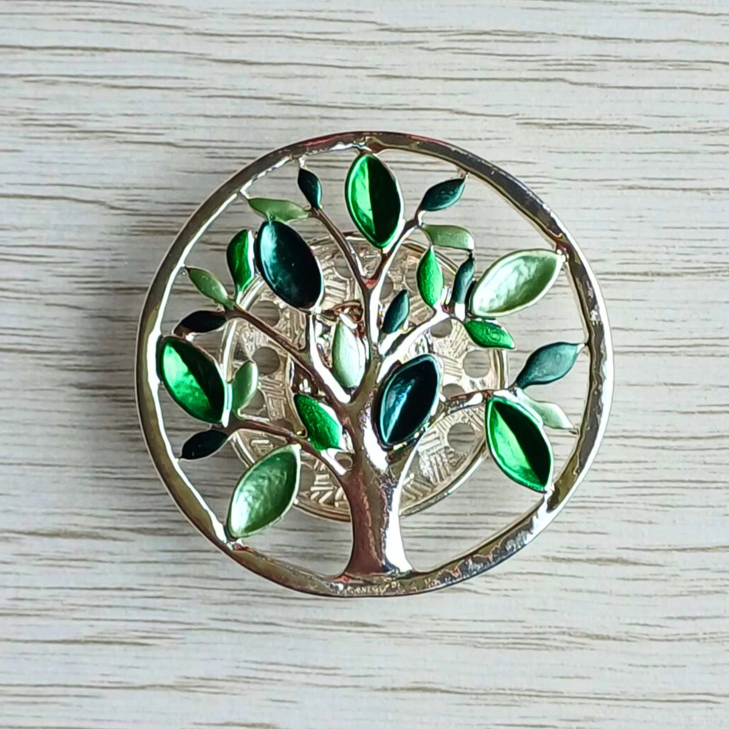 Tree of Life magnetic brooch with green leaves on a wooden surface.
