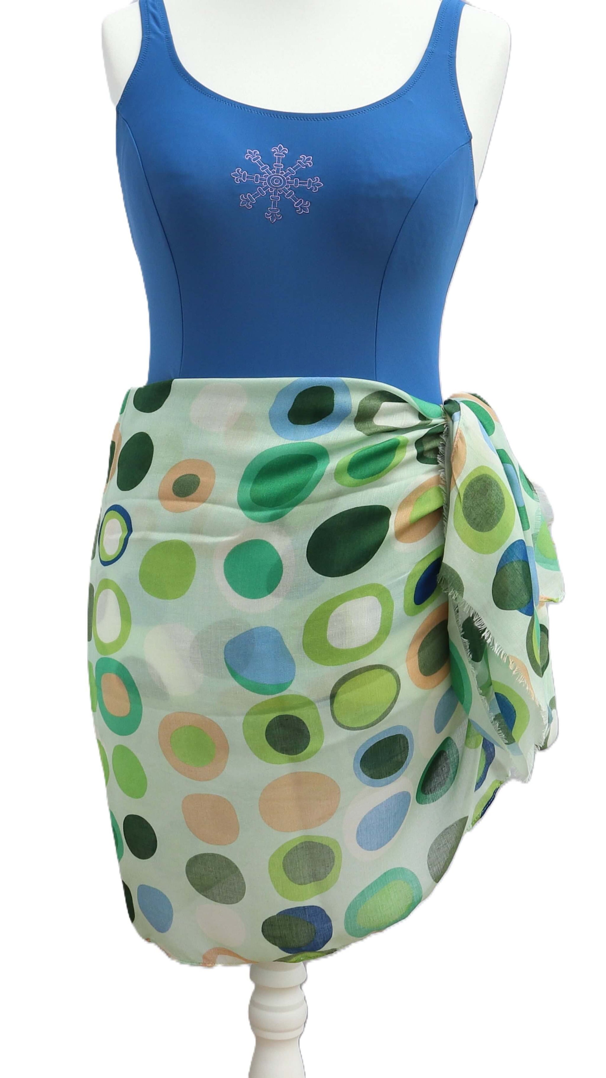 Pale aqua beach wrap with a playful circle and oval pattern in green, peach, and blue tones. Sheer, breezy fabric knotted at the side.
