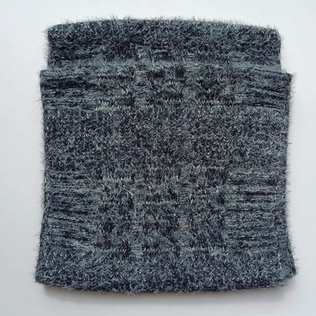 Folded charcoal grey Aran-style knitted snood scarf showing its cable-knit pattern
