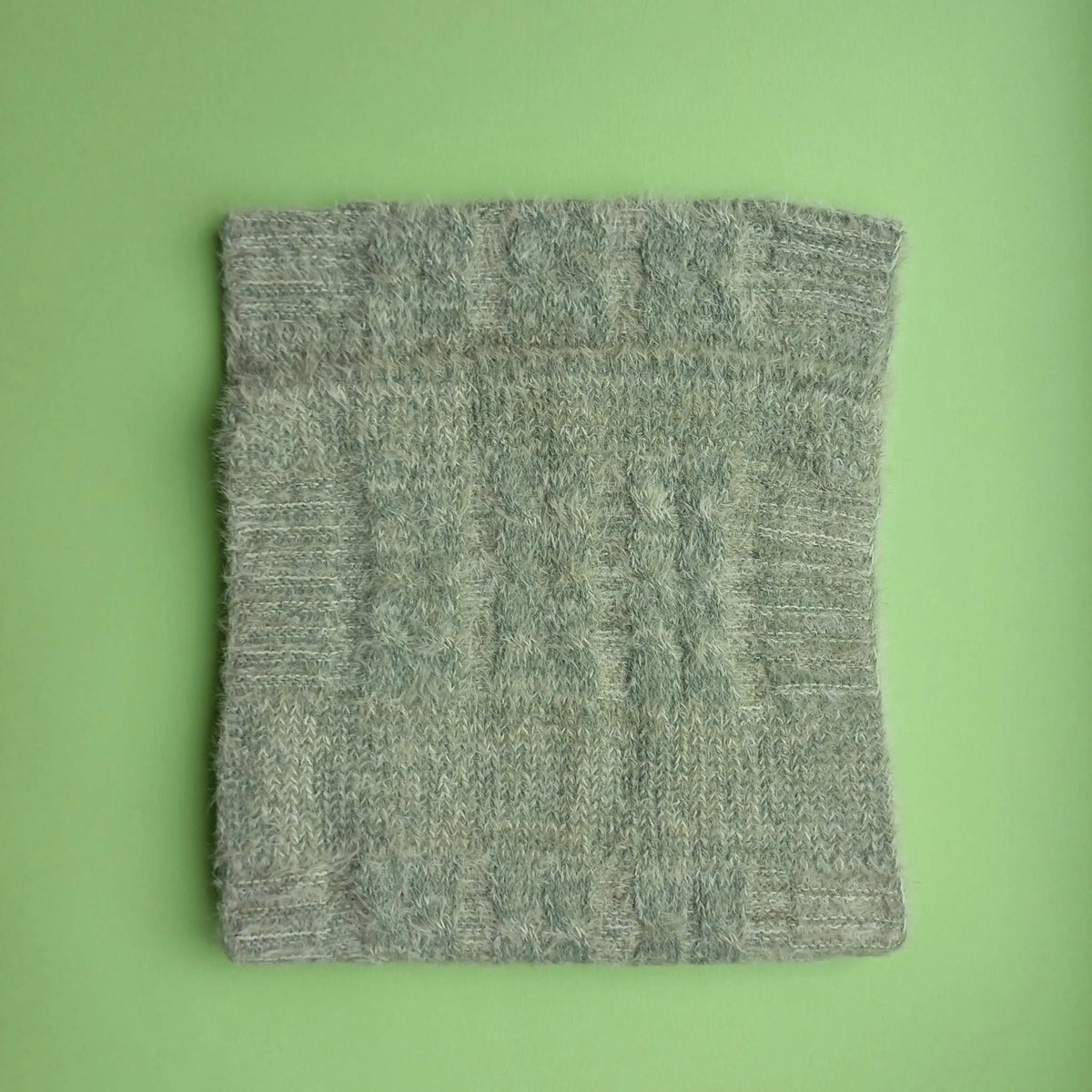 Folded sage green Aran-style knitted snood scarf showing its cable-knit pattern