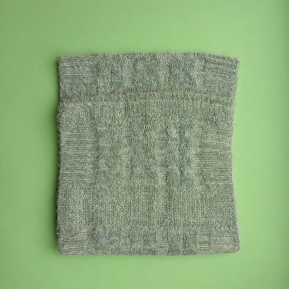 Folded sage green Aran-style knitted snood scarf showing its cable-knit pattern