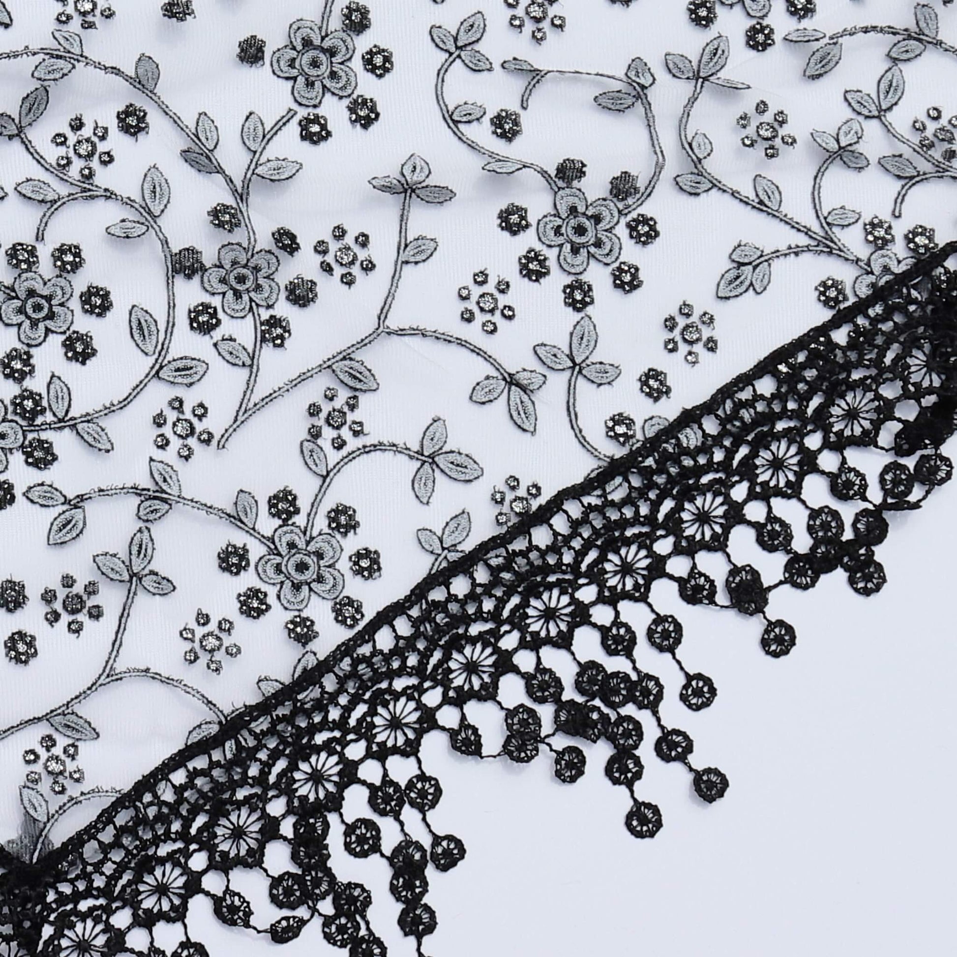 Aurora's Array Glitter Triangle Scarf with Lace & Embroidery (Close-up): A detailed close-up of a white, sheer fabric with delicate grey floral embroidery accented with subtle glitter. The edge features intricate black lace trim with dangling embroidered 