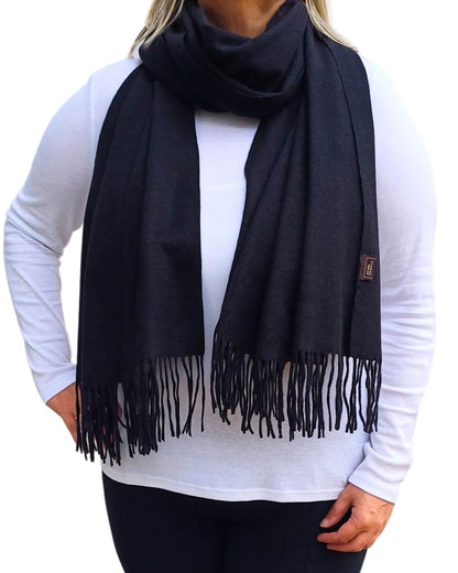 Aurora's Array: Woman models a soft, warm black wool blend scarf with fringed edges, draped around her neck and shoulders.