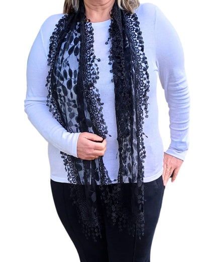 Aurora's Array: Woman models a sophisticated black lace scarf with a delicate leaf pattern and fringed edges.