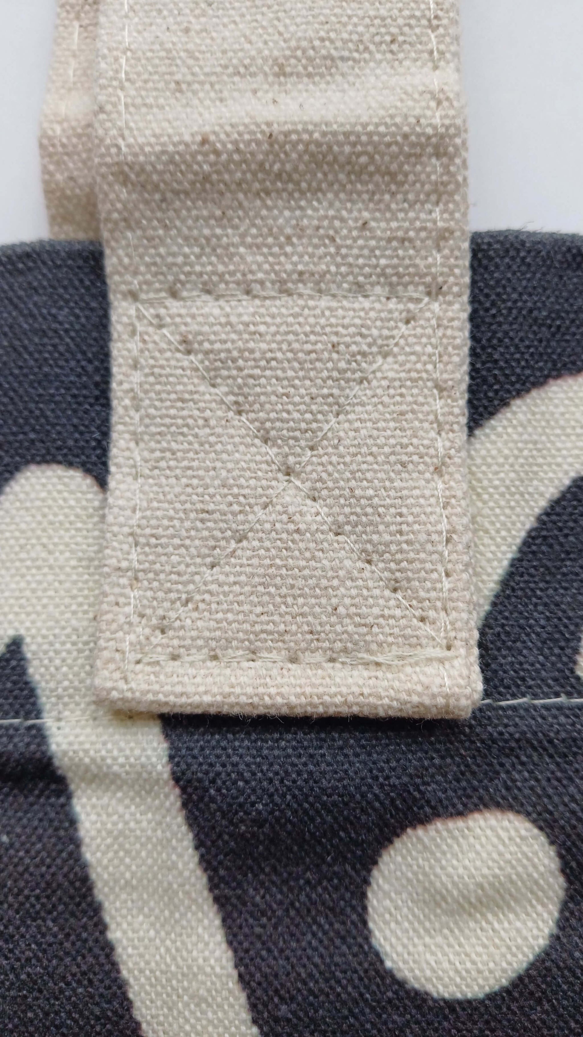 Close-up of a cream-colored canvas handle securely stitched with white thread to a black graffiti-print tote bag. Durable fabric detail.