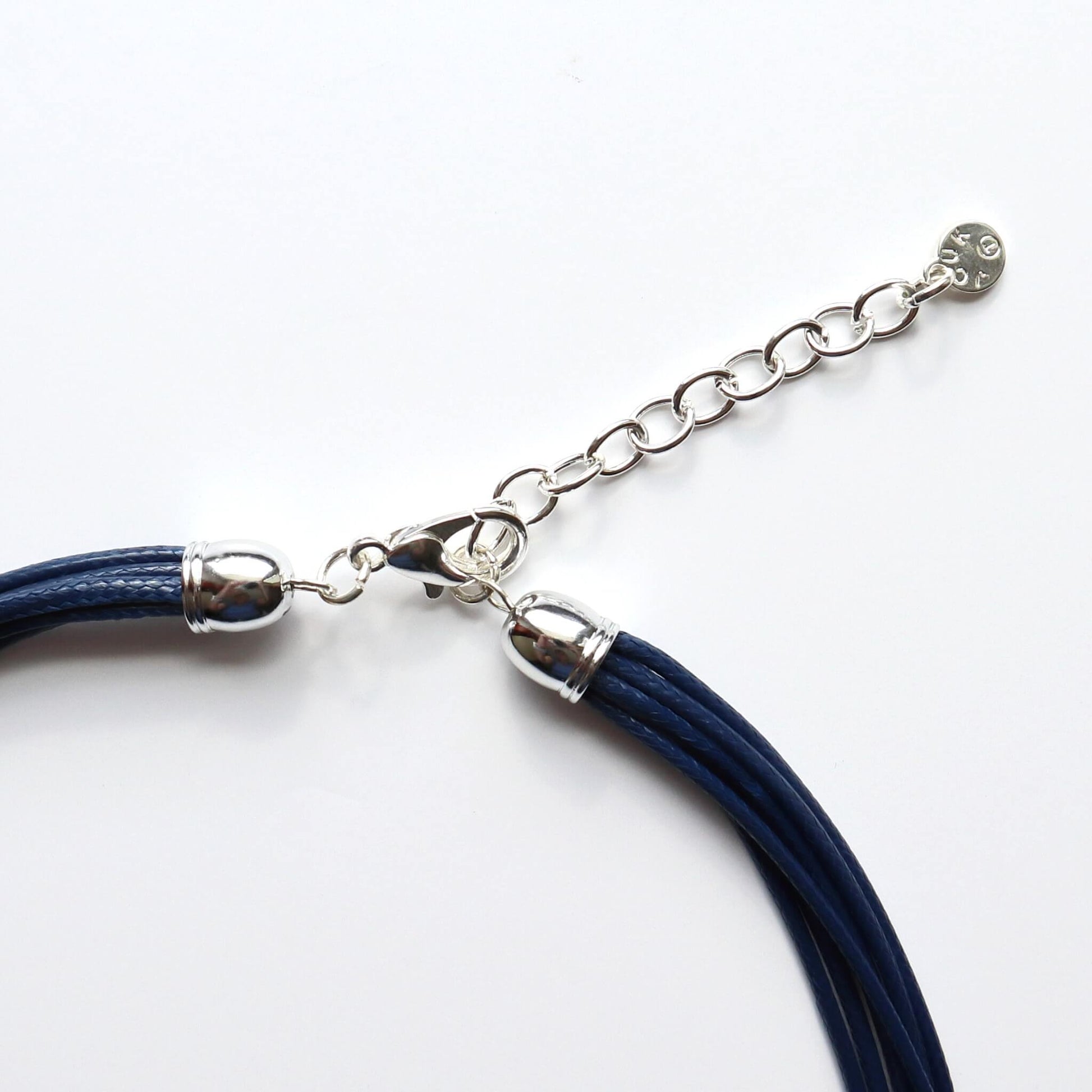 Close-up of a silver-toned necklace clasp and extender chain connected to multiple navy blue cords. Features a lobster claw closure and a small charm.