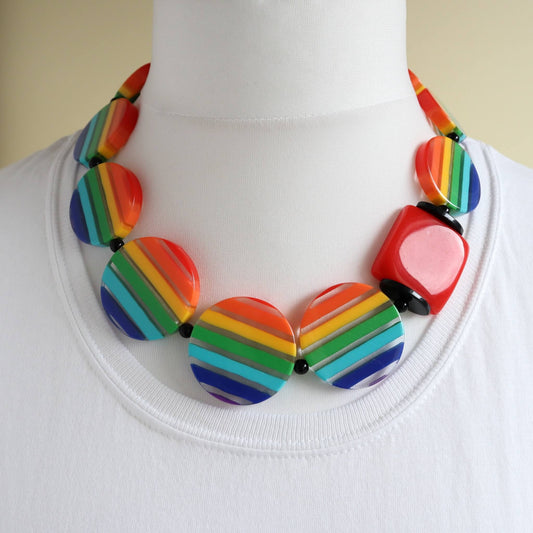 Bold statement necklace with colourful rainbow striped round and square acrylic beads. Features black spacer beads. Fun and vibrant jewellery.
