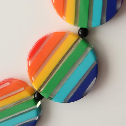Close-up of a bold statement necklace featuring colourful rainbow striped round acrylic beads and black spacer beads. Vibrant and playful.