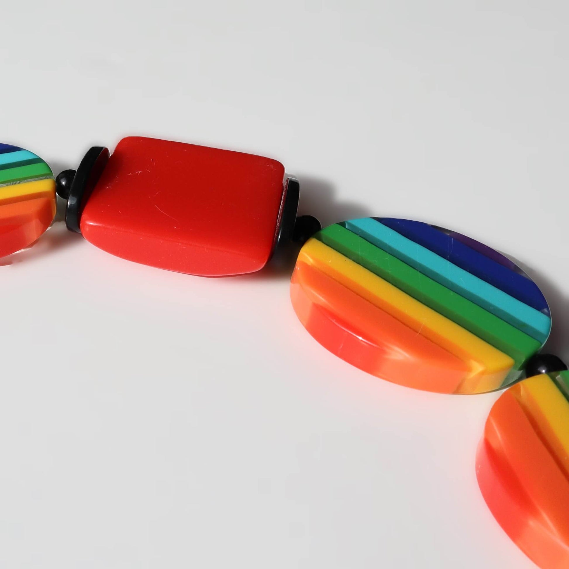 Detailed view of a statement necklace featuring colourful rainbow striped round beads and a solid red rectangular bead. Black spacer beads are visible.