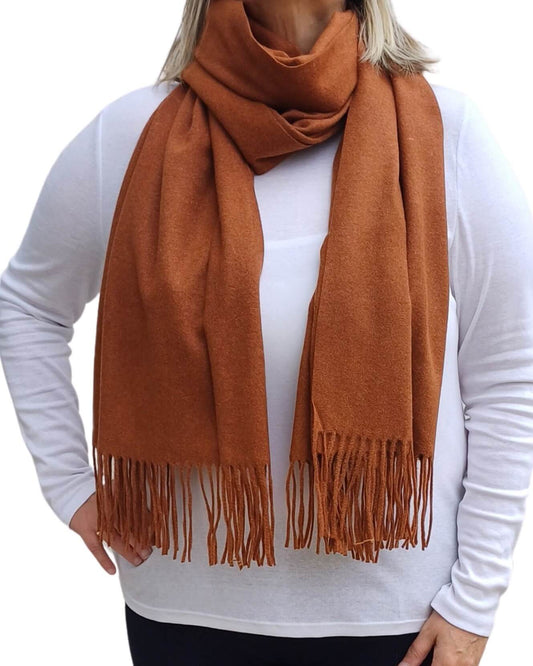 Aurora's Array: Woman models a soft, warm caramel, camel brown wool blend scarf with fringed edges, draped around her neck and shoulders.
