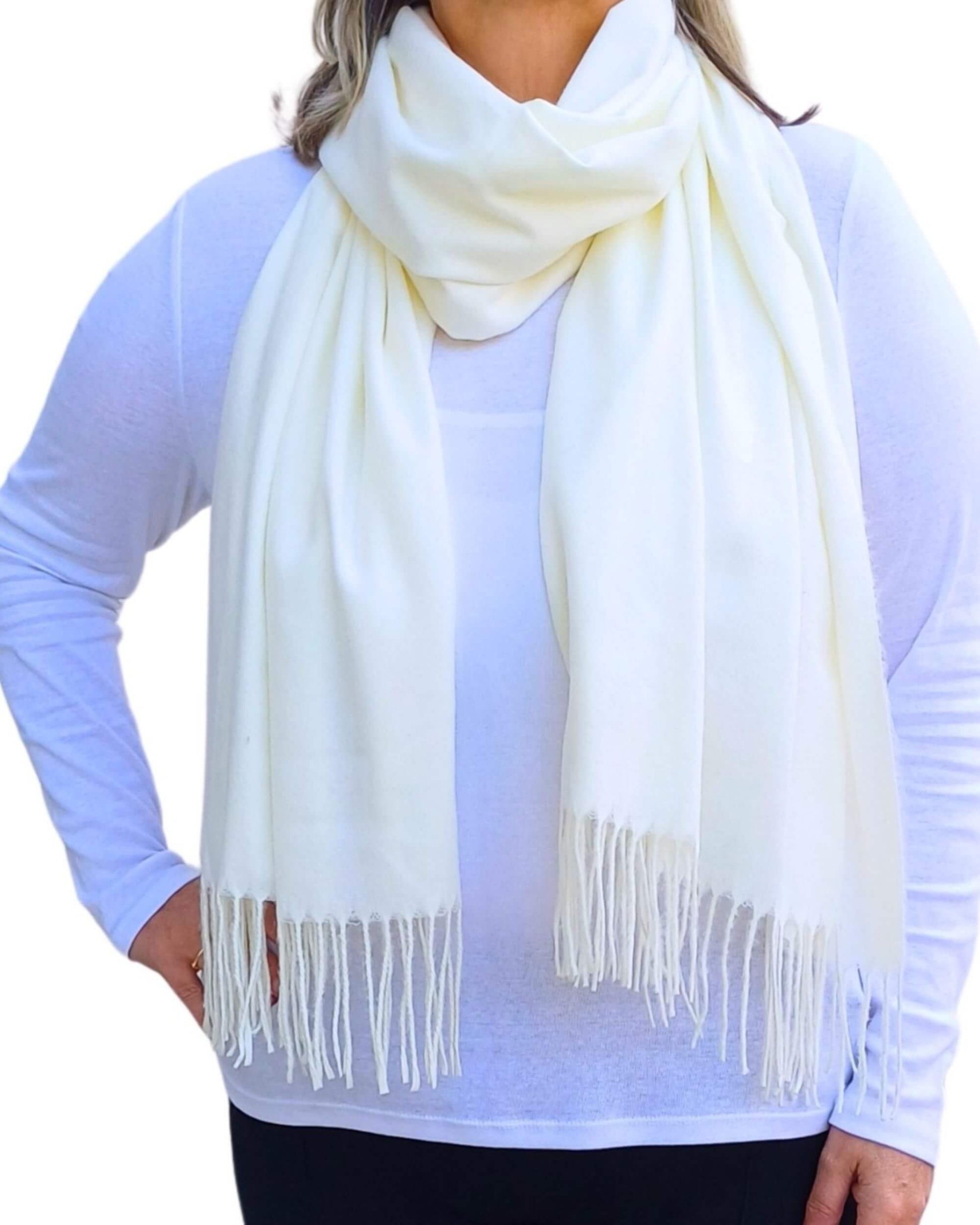 Aurora's Array: Woman models a soft, warm off-white, cream wool blend scarf with fringed edges, wrapped around her neck.